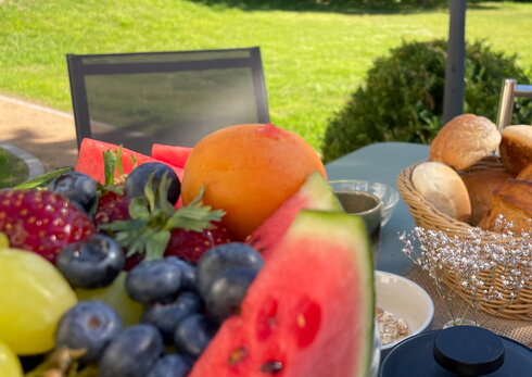 Eingedeckte Obstschale, Kaffee und Brötchenkorb mit Blick in den Garten