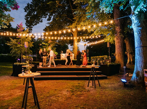 Stimmungsvolle Abendveranstaltung mit Gästen und dekorativen Feuersäulen im beleuchteten Schlosspark von Schloss Kaarz.